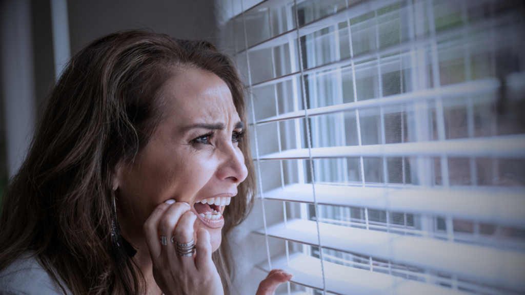 A picture of a woman looking out of a window with a terrified look on her face